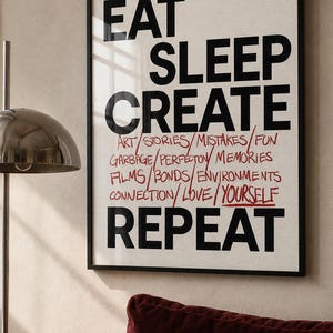 May include: A framed wall art print featuring the bold black text EAT SLEEP CREATE REPEAT. Between the words CREATE and REPEAT, smaller red text lists: ART, STORIES, MISTAKES, FUN, GARBAGE, PERFECTON, MEMORIES, FILMS, BONDS, ENVIRONMENTS, CONNECTION, LOVE, YOURSELF.