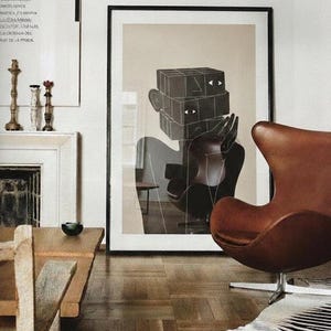 May include: A framed art print featuring a black and white abstract figure with a geometric head. A brown leather armchair and a zebra-print rug are in the foreground. The room has hardwood floors and a neutral color palette.