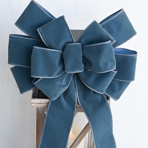 May include: A large teal blue velvet bow with a wired edge. The bow is tied around a wooden lantern and is accented with white flowers.