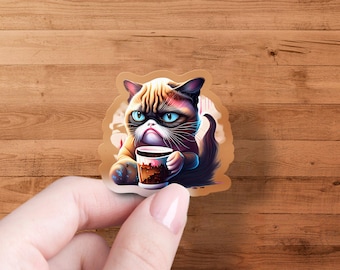 May include: A grumpy-looking cat with brown, white, and black fur is holding a brown and white coffee mug. The cat is sitting on a white background with a blue and purple design.