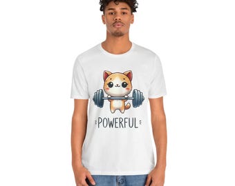 May include: White t-shirt featuring a cartoon cat lifting a barbell. The cat is orange and white with large eyes. The word "POWERFUL" is printed below the cat in a playful font. The shirt is a casual style.