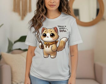 May include: Light gray t-shirt featuring a cartoon cat holding a knife. The cat is tan and white with large eyes and a yellow scarf. Text on the shirt reads, "Silence is golden... Stfu."