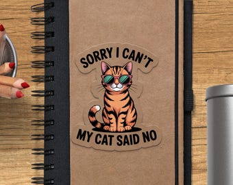 Könnte beinhalten: Ein Aufkleber mit einer Cartoon-Katze mit Sonnenbrille. Die Katze ist orange und schwarz, mit dem Text "SORRY I CAN'T MY CAT SAID NO" in einer geschwungenen Schriftart über und unter der Katze. Der Aufkleber befindet sich auf einem braunen Notizbuch.