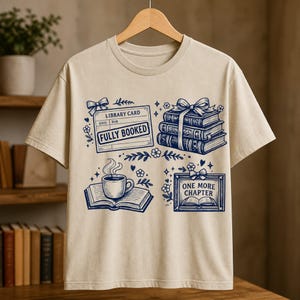 Peut inclure: Un t-shirt beige avec une impression graphique bleu foncé représentant une fiche de bibliothèque marquée FULLY BOOKED, une pile de trois livres avec un ruban, une tasse de café fumante sur un livre ouvert et un cadre marqué ONE MORE CHAPTER.