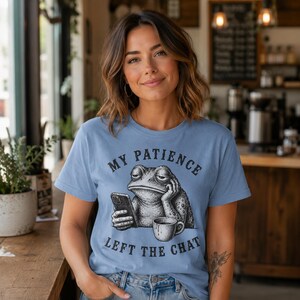 May include: A light blue t-shirt featuring a black and white graphic of a toad resting its head on one hand while holding a smartphone. Below the toad is a coffee mug. The text "MY PATIENCE LEFT THE CHAT" is printed in a curved font around the graphic.