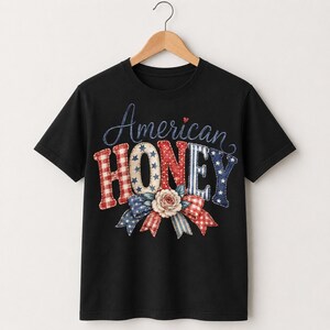 Peut inclure: Un t-shirt noir à manches courtes avec le texte American HONEY dans une police stylisée. Les lettres sont décorées de motifs rouges, blancs et bleus incluant des étoiles, des rayures et du vichy. Un nœud floral orne le mot HONEY.