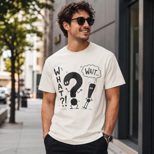 Peut inclure: Un t-shirt à manches courtes de couleur crème avec une impression graphique noire représentant un personnage en forme de point d'interrogation avec le texte "WHAT?!" et un point d'exclamation avec une bulle contenant "WAIT..." style dessin.