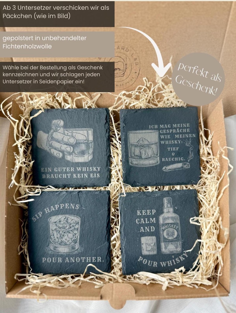 May include: A set of four square slate coasters with engraved whiskey-themed designs and phrases. The coasters are packaged in a cardboard box with decorative straw. Phrases include "Ein Guter Whisky Braucht Kein Eis" and "Keep Calm and Pour Whisky."