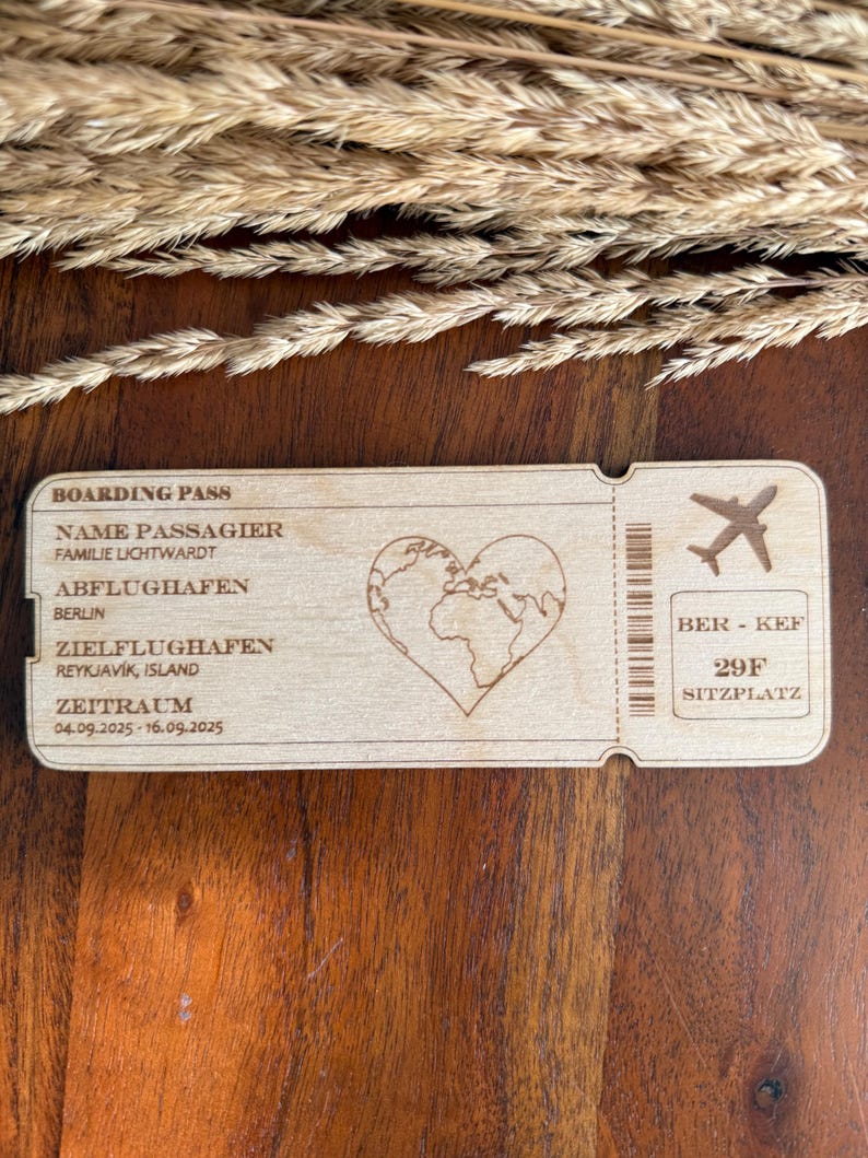 May include: A wooden boarding pass with the text "BOARDING PASS", "NAME PASSAGIER", "FAMILIE LICHTWARDT", "ABFLUGHAFEN", "BERLIN", "ZIELFLUGHAFEN", "REYKJAV&Iacute;K, ISLAND", "ZEITRAUM", "04.09.2025-16.09.2025", "BER - KEF", "29F", "SITZPLATZ". The pass features a heart-shaped world map and a small airplane icon.