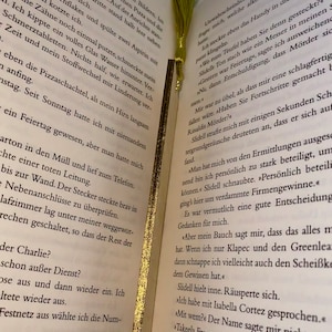 May include: A close-up of an open book with a yellow bookmark. The book is open to a page with text about a murder investigation. The text includes the names "Slidell" and "Rinaldis".
