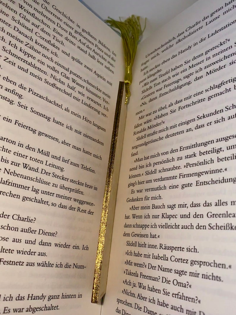 May include: A close-up of an open book with a yellow bookmark. The book is open to a page with text about a murder investigation. The text includes the names "Slidell" and "Rinaldis".