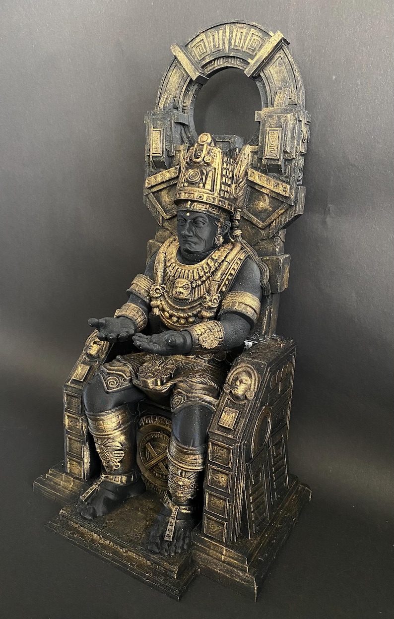 May include: A black and gold statue of a seated figure wearing a crown and elaborate jewelry. The figure is sitting on a throne with intricate carvings. The statue is made of a durable material and is a great addition to any home decor.