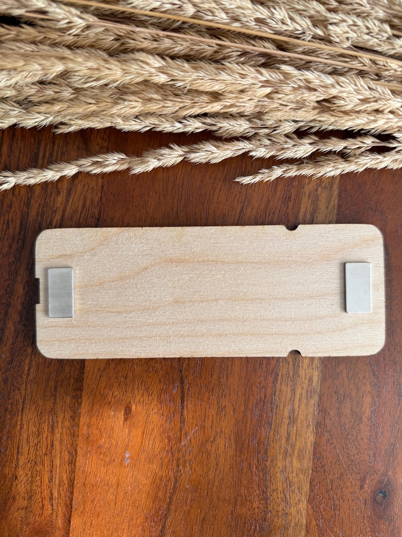 May include: A rectangular wooden sign with a natural wood finish. The sign has two silver metal magnets on the back.