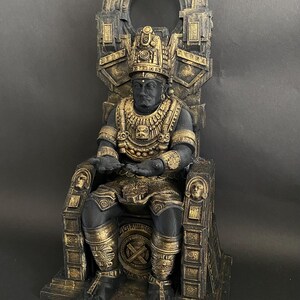 May include: A black and gold statue of a figure sitting on a throne. The figure is wearing a crown and elaborate jewelry. The throne is ornately decorated with carvings and designs.