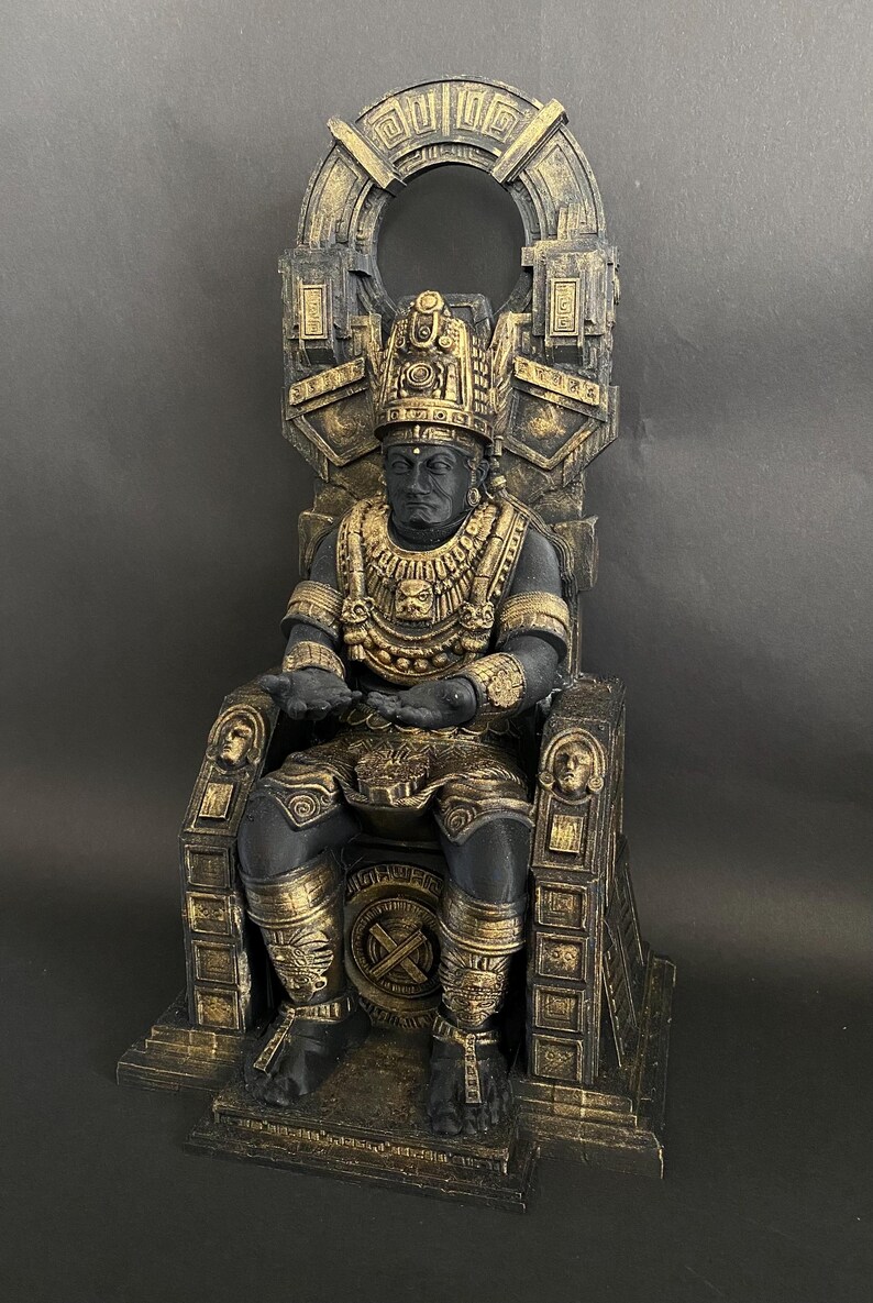 May include: A black and gold statue of a figure sitting on a throne. The figure is wearing a crown and elaborate jewelry. The throne is ornately decorated with carvings and designs.