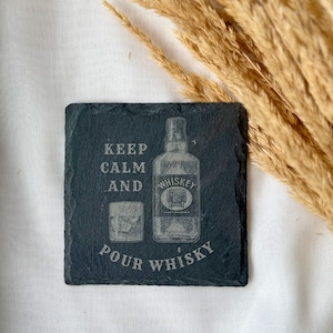 May include: A square, dark gray slate coaster with the words "KEEP CALM AND POUR WHISKEY" etched into the surface. The design includes an illustration of a whiskey bottle and a glass of whiskey.