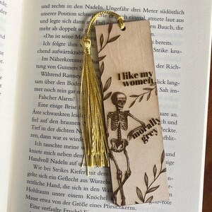May include: A wooden bookmark with a skeleton illustration and the text "I like my women morally grey". The bookmark has a gold tassel and a floral design.