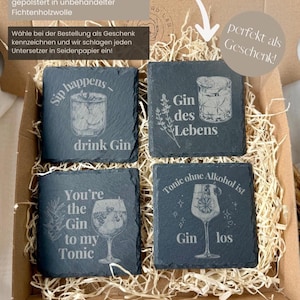 May include: Four square slate coasters with engraved cocktail designs and phrases like "Sip happens - drink Gin" and "You're the Gin to my Tonic." The coasters are packaged in a cardboard box with straw.
