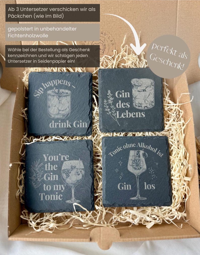 May include: Four square slate coasters with engraved cocktail designs and phrases like "Sip happens - drink Gin" and "You're the Gin to my Tonic." The coasters are packaged in a cardboard box with straw.