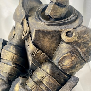 May include: A gold-painted, 3D printed, robot figurine with a detailed, textured surface. The robot is standing on a black base.