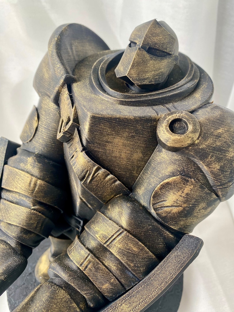 May include: A gold-painted, 3D printed, robot figurine with a detailed, textured surface. The robot is standing on a black base.