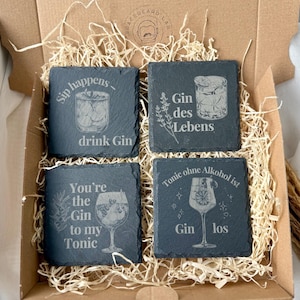May include: A set of four square slate coasters with engraved gin-themed designs and phrases, including "Sip happens - drink Gin" and "You're the Gin to my Tonic." The coasters are presented in a cardboard box with straw.