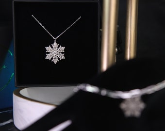 May include: A silver snowflake pendant necklace in a black velvet box. The snowflake is made of small, clear stones.