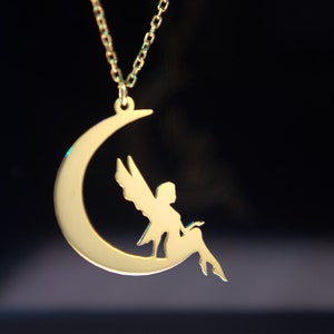 May include: A gold necklace with a crescent moon pendant featuring a fairy silhouette sitting on the moon.