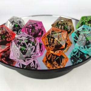 May include: A collection of colorful, faceted dice with compass designs inside. The dice are in various colors, including red, pink, orange, green, and teal. The dice are displayed on a reflective surface, creating a mirrored effect. The dice are a unique gaming accessory.