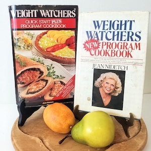 May include: Two Weight Watchers cookbooks, one titled Quick Start Plus Program Cookbook and the other New Program Cookbook by Jean Nidetch, displayed with a yellow lemon and a green pear on a round wooden board.