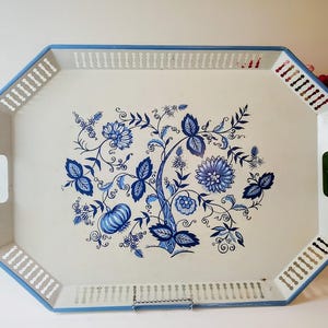 May include: An octagonal serving tray with a white surface and blue trim. The tray features a floral design in shades of blue. The tray has cut-out handles and decorative cut-outs along the edges.
