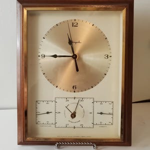 May include: Vintage Airguide clock and weather station in a wooden frame. The clock has a gold-colored face with black hands and numerals. Below are temperature, barometer, and humidity gauges.