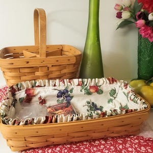 May include: Two rectangular woven wood baskets with light brown finish. One basket features a tall central handle and interior dividers. The other basket is lined with a cream-colored fabric featuring a colorful fruit and berry print pattern.