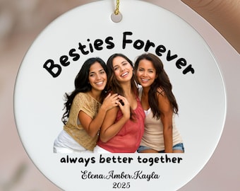 May include: A white ceramic ornament with a gold string, featuring a photo of three smiling women. The text "Besties Forever" and "always better together" are above and below the photo, with names and the year 2025 below.
