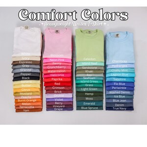 Może przedstawiać: Stosy złożonych, ciężkich koszulek unisex Comfort Colors w r&oacute;żnych kolorach, w tym białym, r&oacute;żowym, zielonym i niebieskim. Obraz przedstawia szeroką gamę odcieni, od jasnych pasteli po głębokie, nasycone tony, z nazwami kolor&oacute;w.