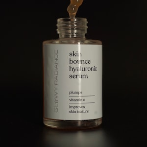 K&ouml;nnte beinhalten: Eine klare Glasflasche mit einer Pipette, gef&uuml;llt mit einer hellbraunen Fl&uuml;ssigkeit. Die Flasche ist mit "skin bounce hyaluronic serum" beschriftet und listet die Vorteile als "plumps, vitamin c, improves skin texture" auf. Die Flasche ist mit "Glowy Radiance" beschriftet.