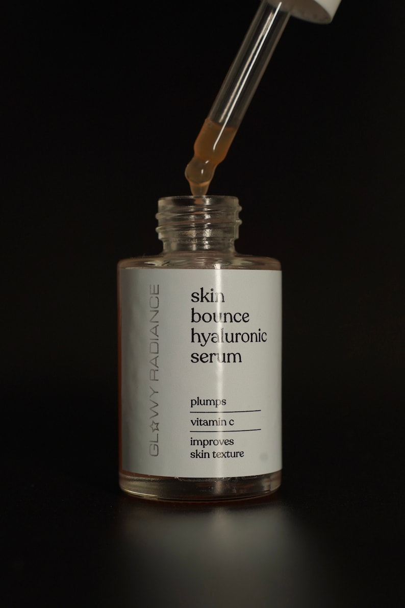 K&ouml;nnte beinhalten: Eine klare Glasflasche mit einer Pipette, gef&uuml;llt mit einer hellbraunen Fl&uuml;ssigkeit. Die Flasche ist mit "skin bounce hyaluronic serum" beschriftet und listet die Vorteile als "plumps, vitamin c, improves skin texture" auf. Die Flasche ist mit "Glowy Radiance" beschriftet.