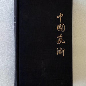 May include: A rectangular hardcover book with a solid black fabric cover. The front cover features vertical gold-colored Chinese characters printed on the right side. The spine is visible on the left edge, showing faint gold text.