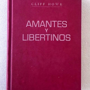 May include: A hardcover book with a deep magenta cover. The text CLIFF HOWE is printed in white at the top, followed by the title AMANTES Y LIBERTINOS in larger white capital letters centered on the front cover. The book has a vertical spine.