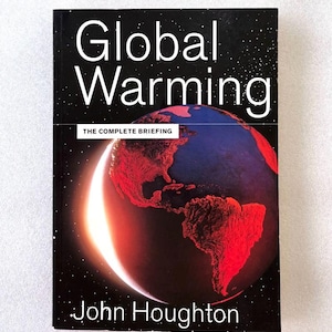 May include: A book titled Global Warming: The Complete Briefing by John Houghton. The black cover features a graphic of the Earth illuminated by a bright crescent light, showing North and South America in red against a dark, starry space background.
