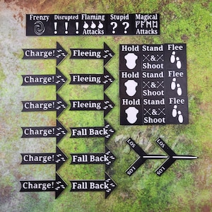 Puede incluir: Un conjunto de fichas de juego negras con texto y símbolos blancos. Las fichas incluyen frases como "Charge!" y "Fleeing", junto con símbolos de acción y descripciones de ataques especiales. El fondo es una superficie verde y herbosa.