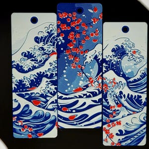 May include: Three rectangular bookmarks with a hole at the top. The designs feature blue and white waves, and red cherry blossoms. The bookmarks are in a Japanese art style.