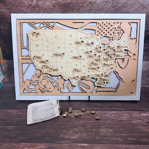 May include: A wooden map of the United States with a football theme. The map is in a white frame and has a small bag of wooden footballs next to it. The map shows the locations of all the NFL stadiums.