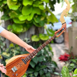 Puede incluir: Un instrumento musical tradicional tailandés llamado "Khim" con un cuerpo de madera tallada y un cuello largo con cabeza de dragón. El instrumento tiene un acabado de madera natural y un conjunto de cuerdas.