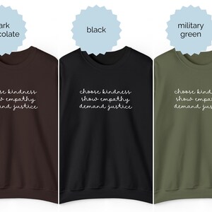 May include: Three crewneck sweatshirts in dark chocolate, black, and military green. Each features white cursive text on the chest that reads: choose kindness, show empathy, demand justice. The sweatshirts have long sleeves and a ribbed neckline.