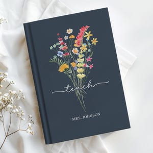 May include: A navy blue journal with a watercolor floral bouquet design. The word "teach" is written in cursive, with "MRS. JOHNSON" below. The flowers are a mix of yellow, red, pink, and blue.