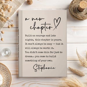 May include: A beige hardcover journal with the words "a new chapter" and a heart symbol in black script. The journal includes inspirational text about courage and building something of your own, signed "Stephanie".