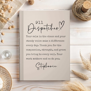 May include: A rectangular beige book with black text that reads 911 Dispatcher, Your calm in the chaos and your steady voice make a difference every day. Thank you for the compassion, strength, and grace you bring to every call. Your work matters and so do you. Stephanie.