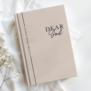 May include: A beige journal with the text "DEAR God" in black script. The spine features the text "LETTERS FROM ASHLEY" in black, with a vertical black line. The journal is on a white surface with floral accents.