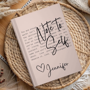 May include: A pink notebook with the text "Note to Self" in black lettering. The notebook has a heart and the name "Jennifer" written in black cursive.
